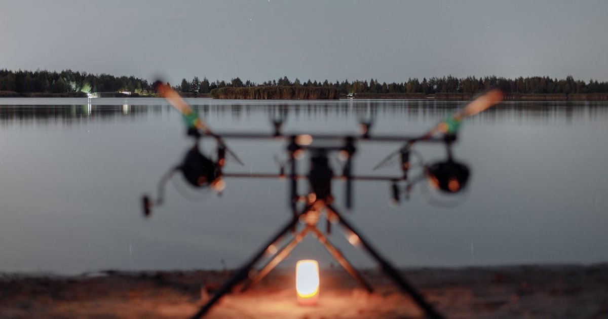 Carpista con bivvy montado junto a un embalse de noche con detectores de picadas encendidos